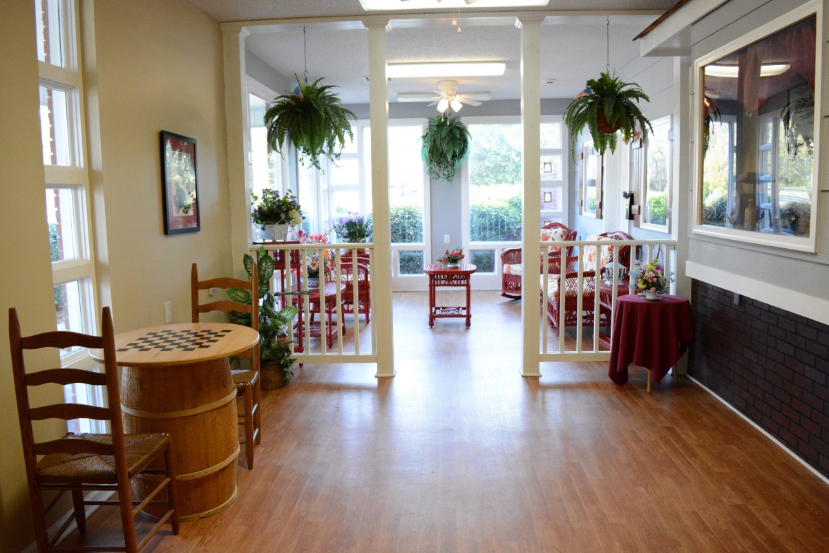 A bright and inviting dining area with wooden floors, featuring tables, chairs, and hanging plants.