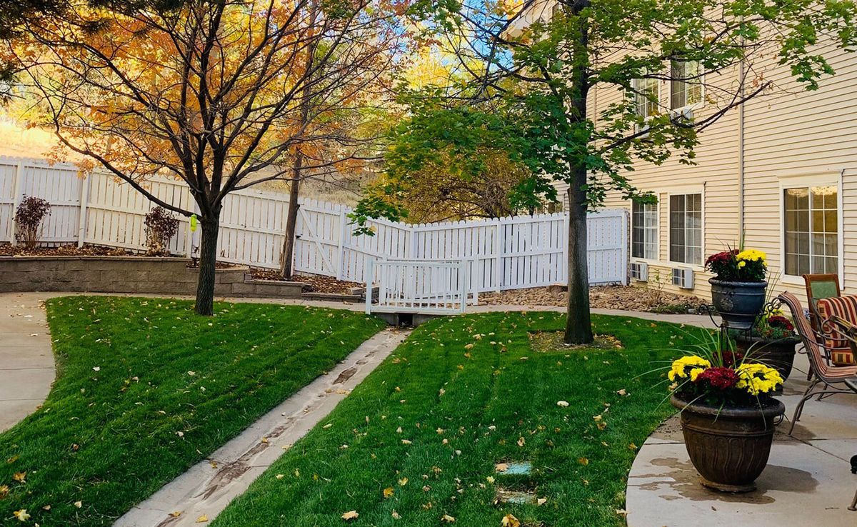 A serene backyard with a white fence, green lawn, and autumn trees.
