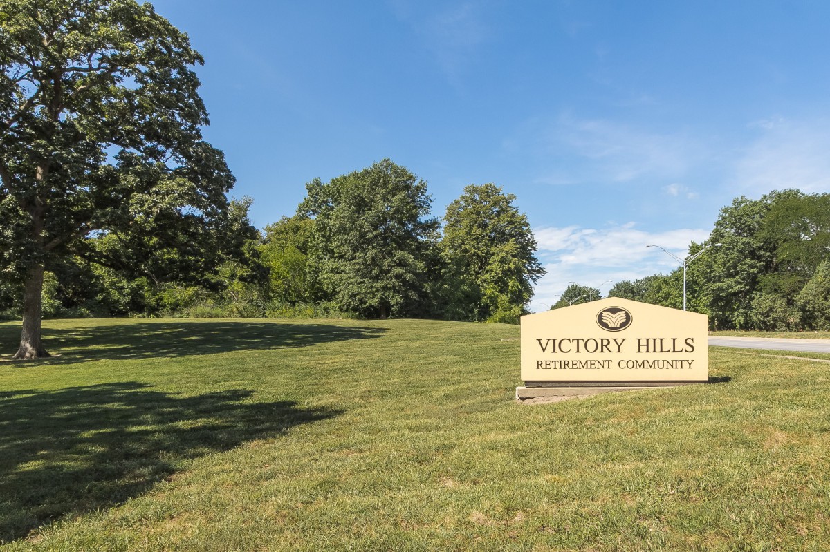 A sign for Victory Hill memorial gardens set in a grassy, tree-lined outdoor area.