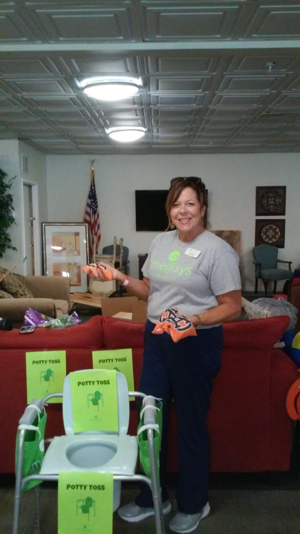 A woman volunteering at a community event, holding toys inside a community center with an American flag in the background.