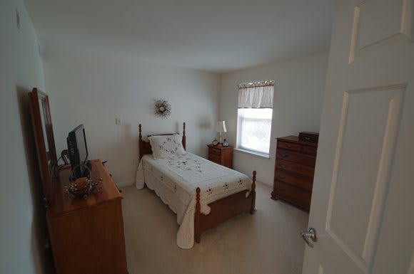 A cozy bedroom with a single bed, dresser, and a window allowing natural light.