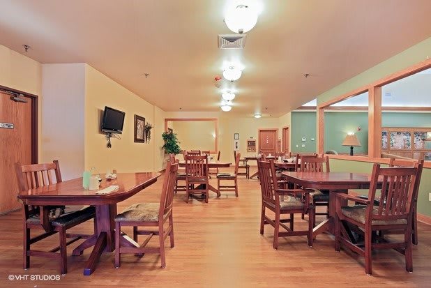 An empty restaurant dining area with wooden tables and chairs, softly lit by ceiling lights.