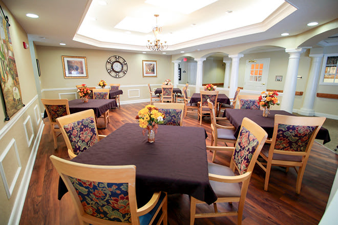 A well-decorated dining room with multiple tables and chairs, featuring floral arrangements and a wooden floor.