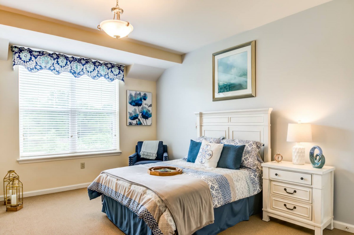 A cozy bedroom with a double bed, blue and white decor, and natural light streaming through the window.