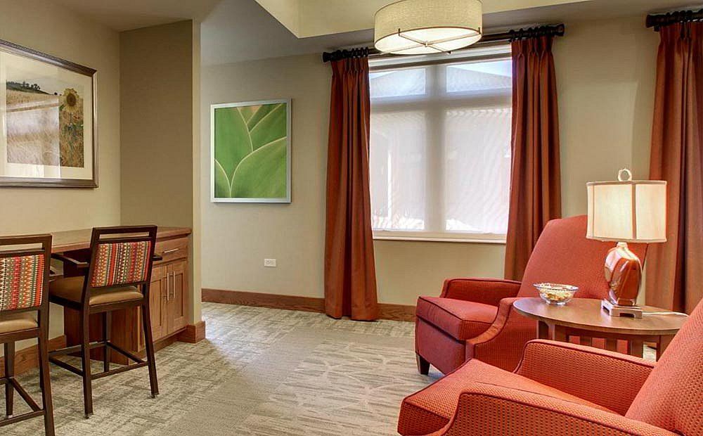 A cozy living room with orange armchairs, a window with curtains, and wall artwork.
