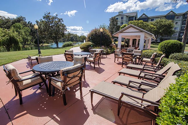A sunny outdoor patio area featuring tables, chairs, and lounge chairs with a gazebo in the background.