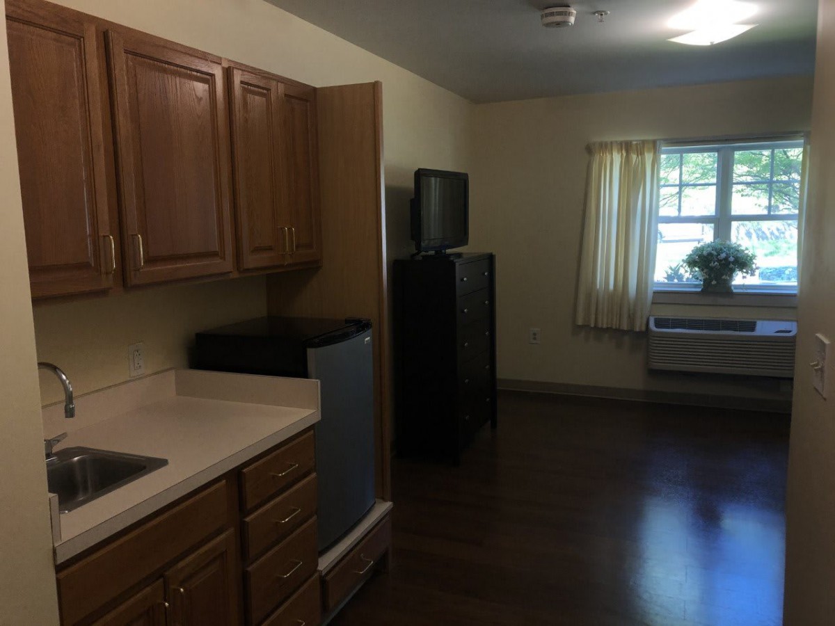 A small kitchen area with wooden cabinets and a window with curtains.