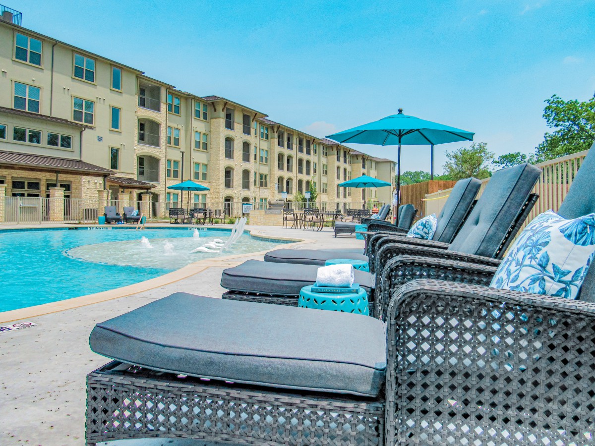 Outdoor pool area with sun loungers and umbrellas at an apartment complex.