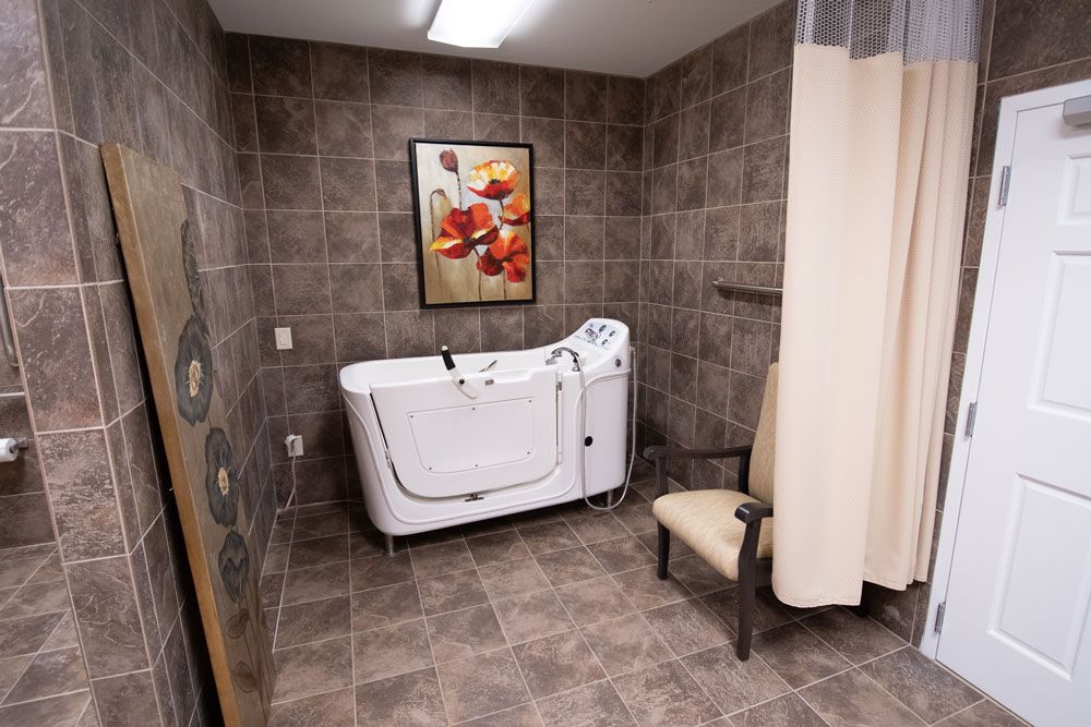 A bathroom featuring an accessible bathtub and a chair with tiled walls.