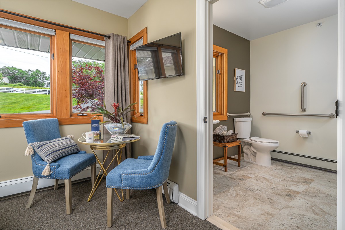 A cozy living area with blue chairs, a small table, and a view into an adjoining bathroom.