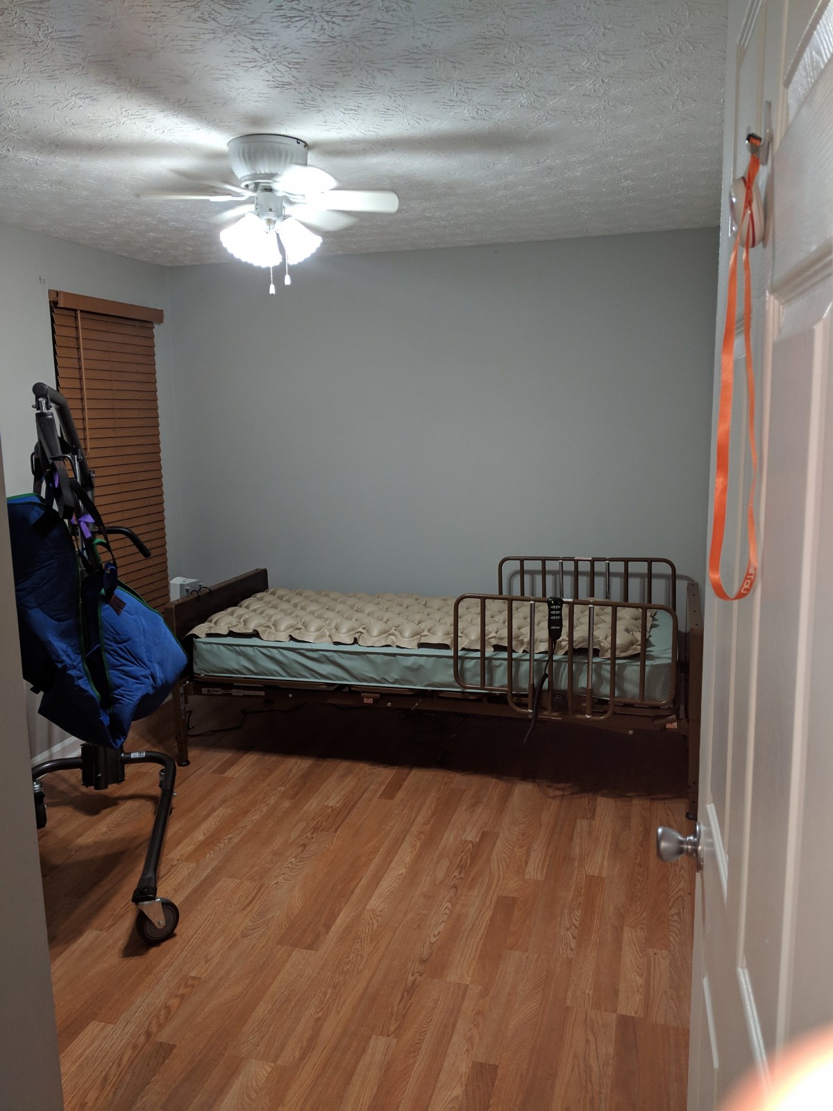 A simple bedroom with a metal bed frame, wooden flooring, and a ceiling fan.