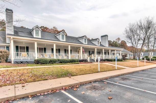 A suburban house with a large front porch and adjacent parking lot.