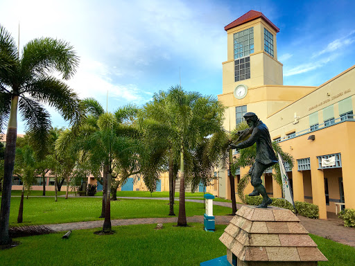 A scenic view of a park featuring a statue, lush palm trees, and a building with a clock tower.