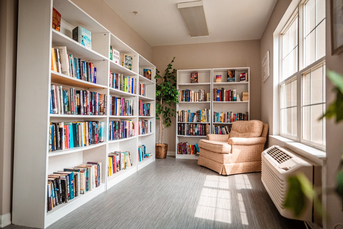 A cozy reading corner in a library with bookshelves filled with books and an armchair by the window.