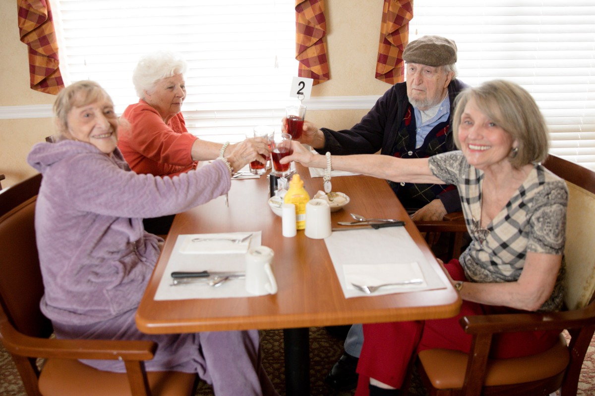 A group of seniors enjoying a meal and toasting together at a dining table.