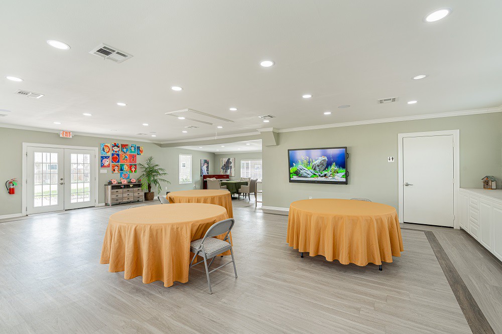 A modern event space with round tables draped in orange cloths, featuring a wall-mounted television and a stylish interior design.