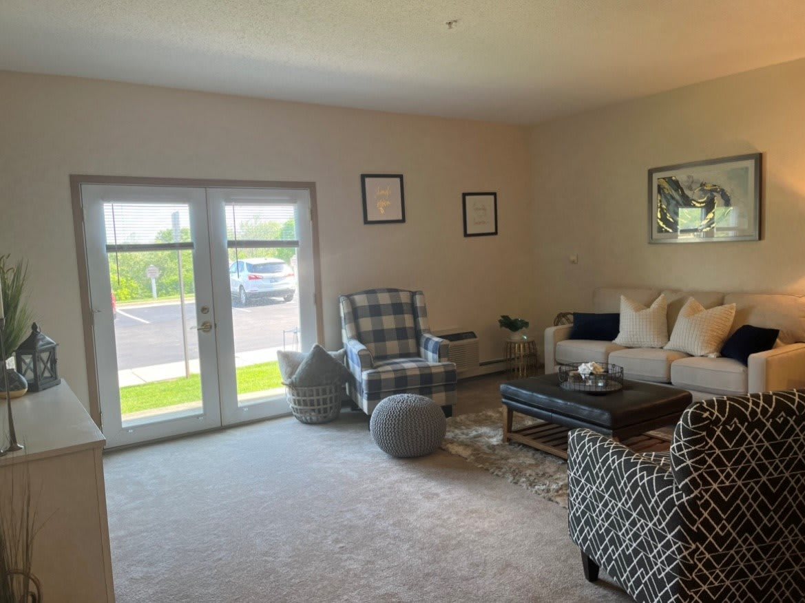 A cozy living room with a sofa, armchairs, and a coffee table, well-lit by natural light through the windows.