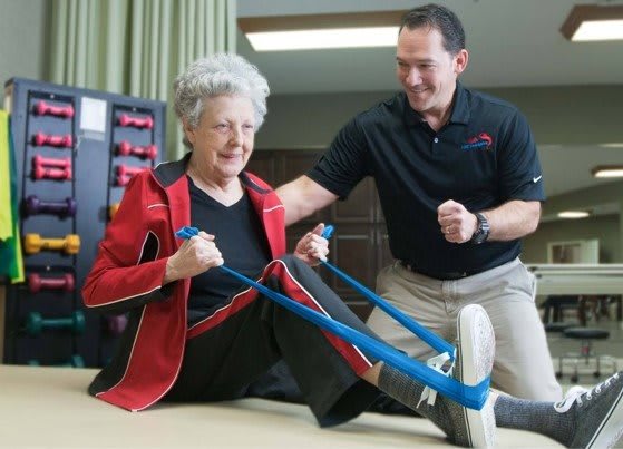 An elderly woman engaging in a physical therapy session with a therapist using a resistance band.