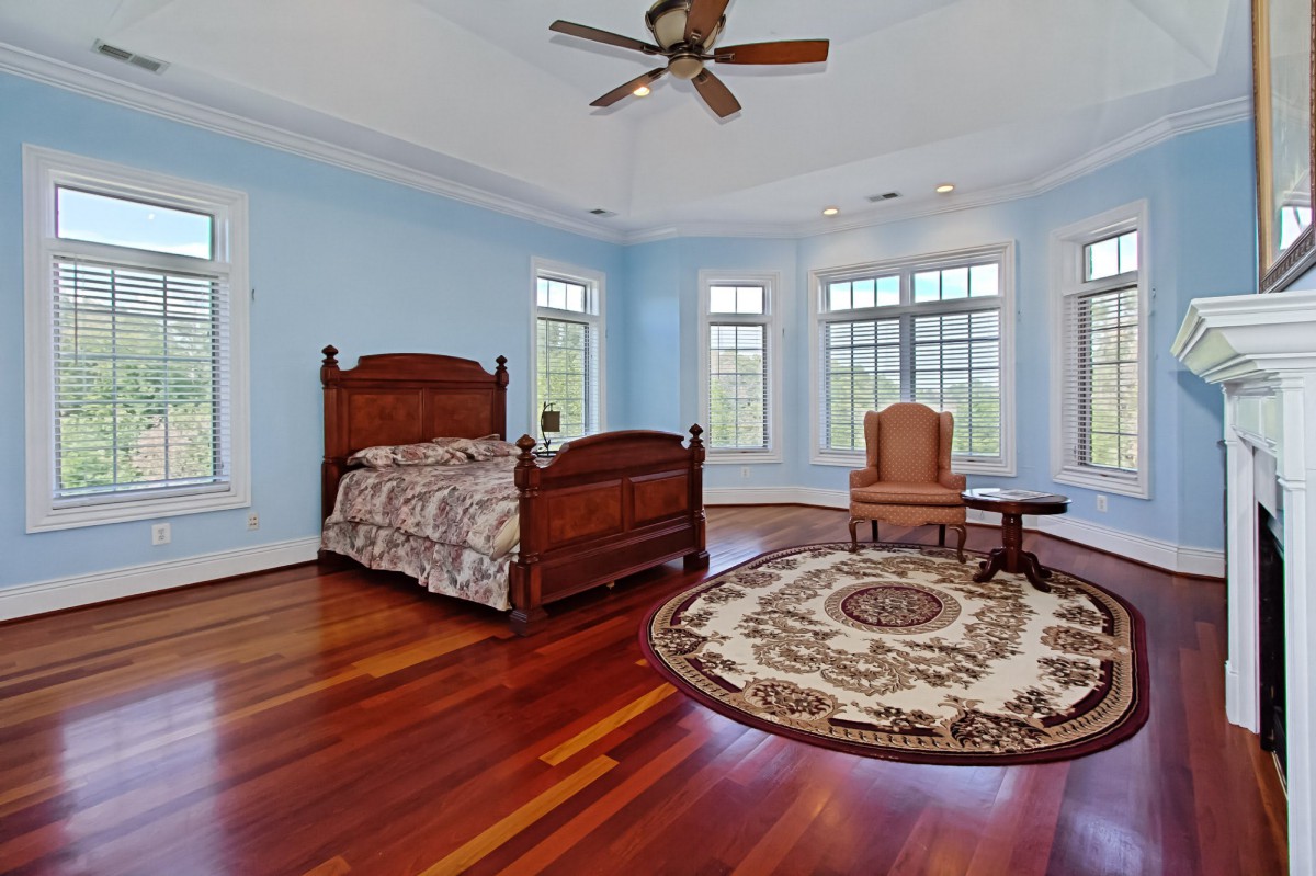 A spacious bedroom with wooden floors and a large rug, featuring a bed and multiple windows for natural light.