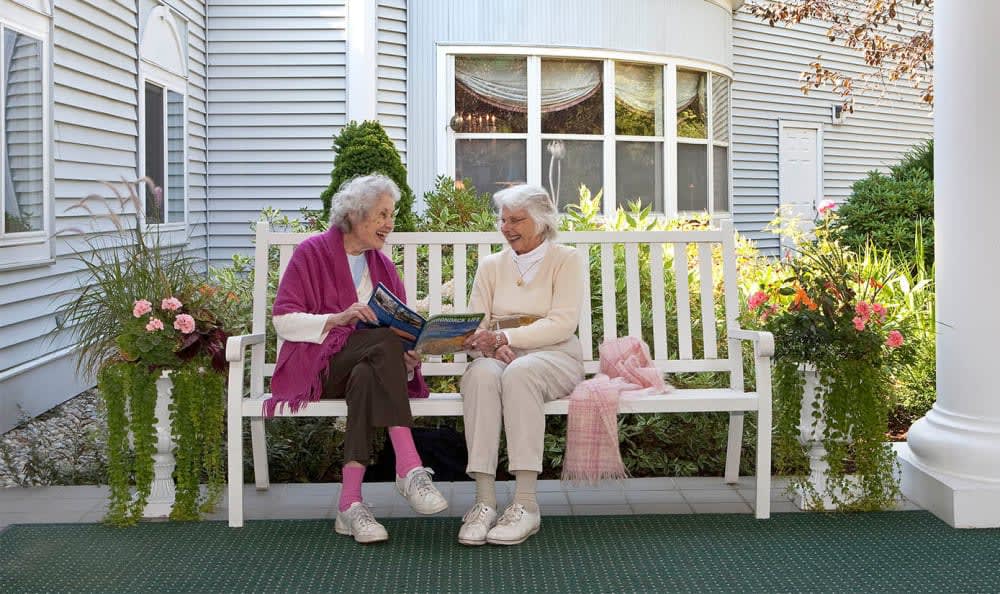 Two elderly women sitting on a bench, engaging in conversation outdoors.