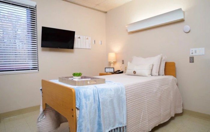 A clean and tidy hospital room with a bed, television, and lamp.