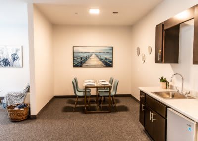 A modern dining area featuring a table with four chairs, artwork on the wall, and a small kitchenette.