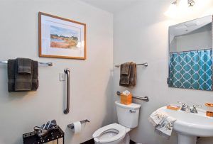 A bathroom featuring a toilet, towels, wall art, and a handrail.