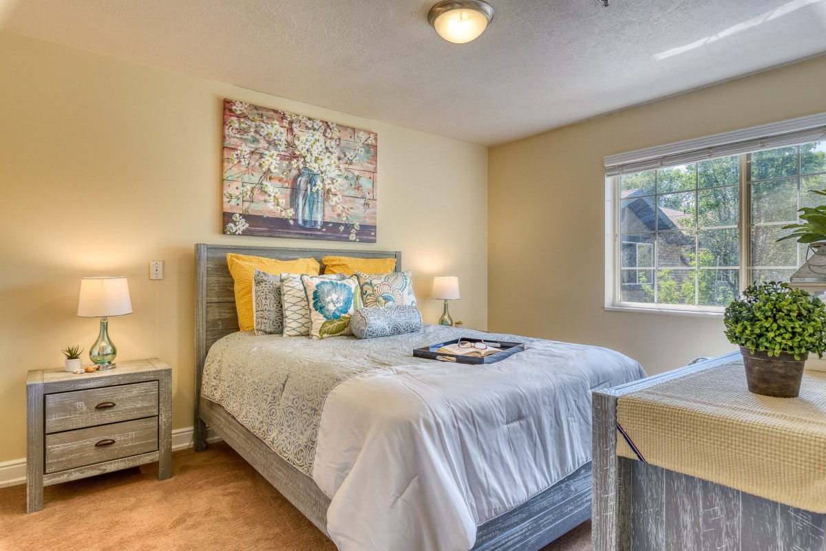 A cozy, well-decorated bedroom featuring a comfortable bed with pillows and a vibrant painting above the headboard.
