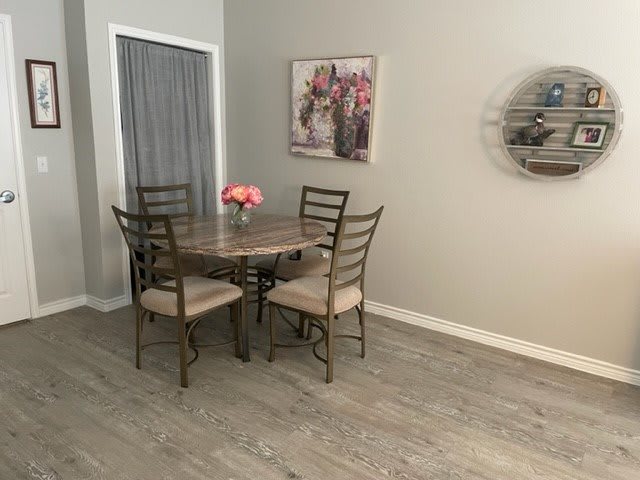 A cozy dining area with a round wooden table, four chairs, and a vase of flowers on the table, accompanied by wall decorations.