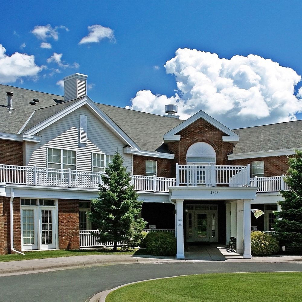 A large residential house with a gabled roof and white railings under a blue sky with clouds.