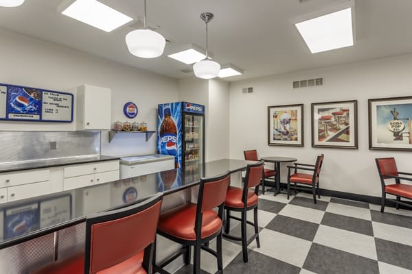 A comfortable break room featuring red chairs, a long table, a vending machine, and checkered flooring.