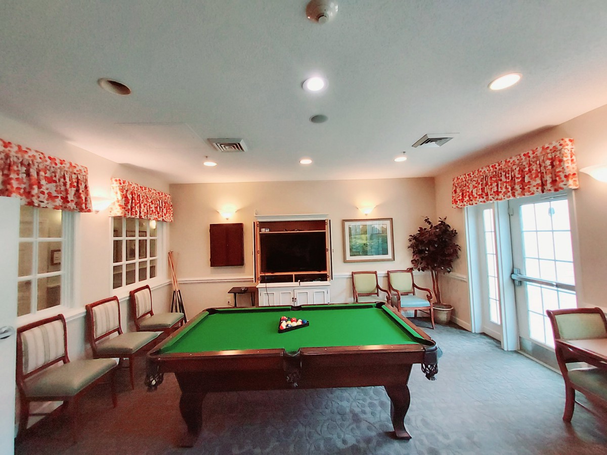 A cozy game room featuring a pool table with green felt, surrounded by decorative chairs and a warm interior.