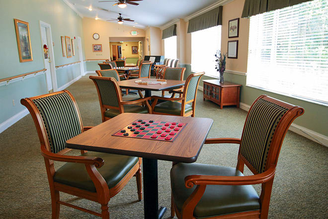 A community room with a checkerboard on the table, surrounded by comfortable seating and large windows.