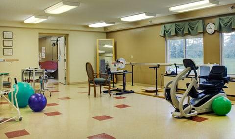 A rehabilitation room with various exercise equipment and furniture.