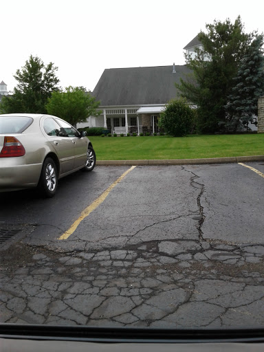 A silver car parked in a lot with a grassy area and a house in the background.