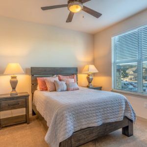 A cozy bedroom with a neatly made bed, flanked by nightstands with lamps, and a ceiling fan overhead.