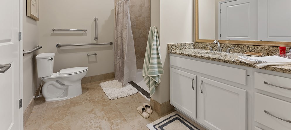 A bathroom featuring a shower with a curtain, towels hanging by the wall, slippers on the floor, and a sink with a cabinet beneath a mirror.