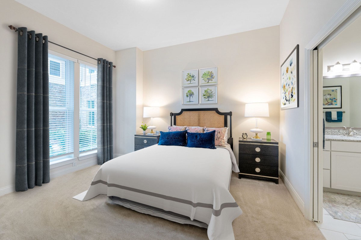 A modern and cozy bedroom featuring a double bed with navy blue pillows, flanked by two nightstands with lamps, and decorated with wall art.