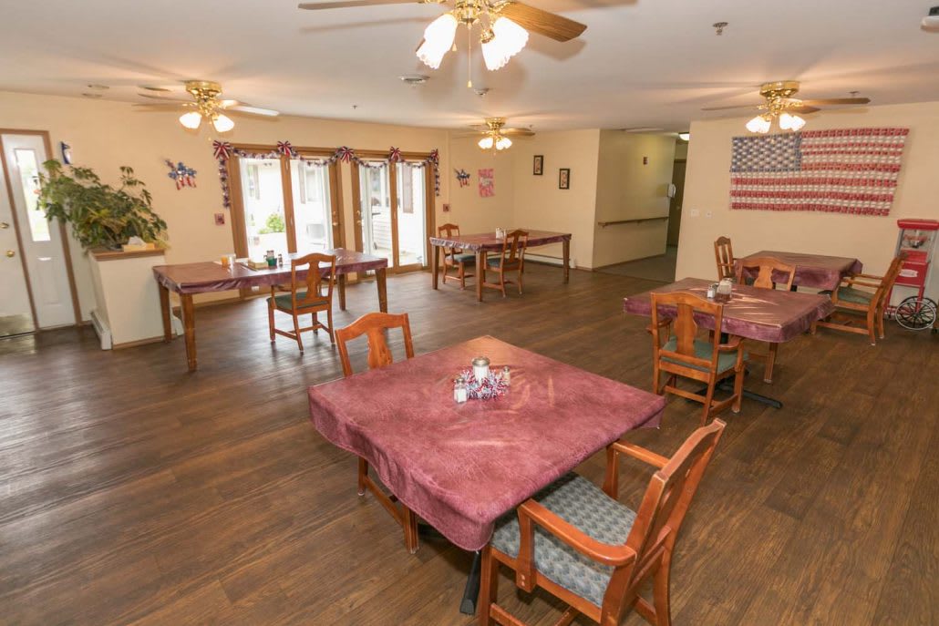 A dining area with neatly arranged tables and chairs, featuring wooden floors and ceiling fans.
