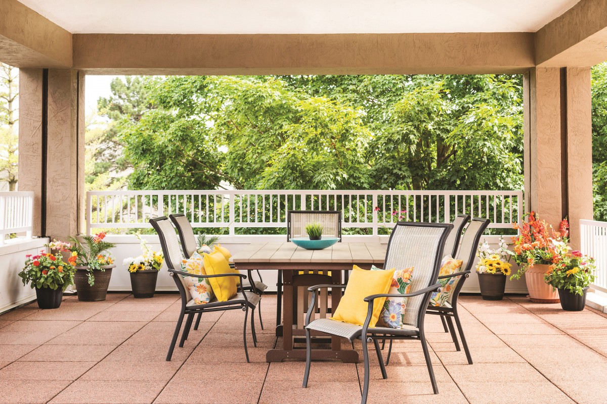 An inviting patio setup with a wooden table, chairs adorned with yellow cushions, and a lush garden view.