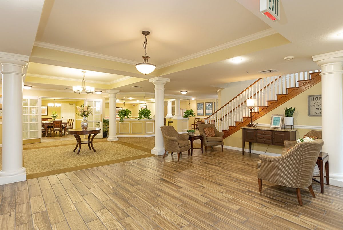 A spacious and elegantly designed lobby featuring hardwood floors, comfortable seating, decorative columns, and a staircase.