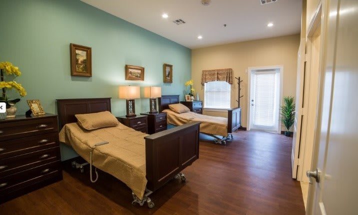 A clean and well-organized hospital room with two medical beds, decorated with paintings and offering a calm environment.