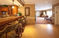 A cozy interior featuring a bar area with seating and warm lighting, leading into a lounge space.