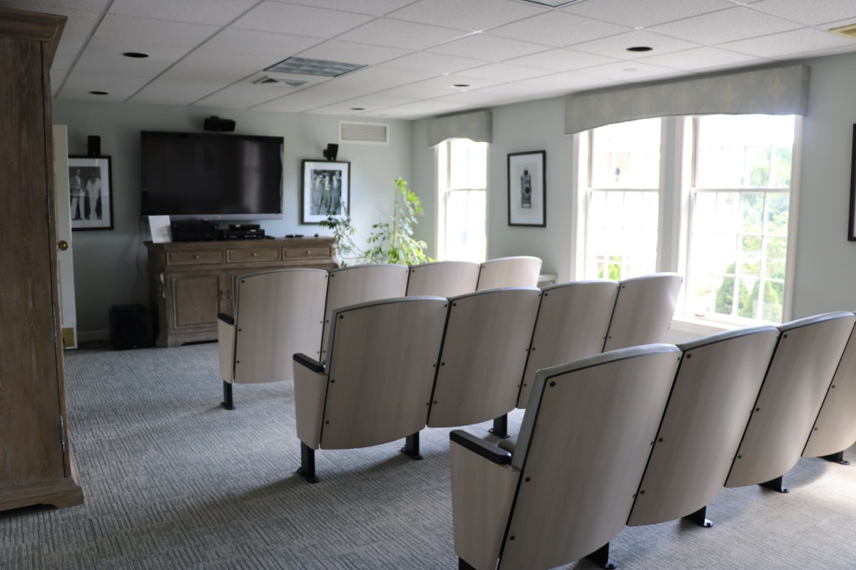 A small conference room with rows of beige chairs facing a podium and a large flat screen television.