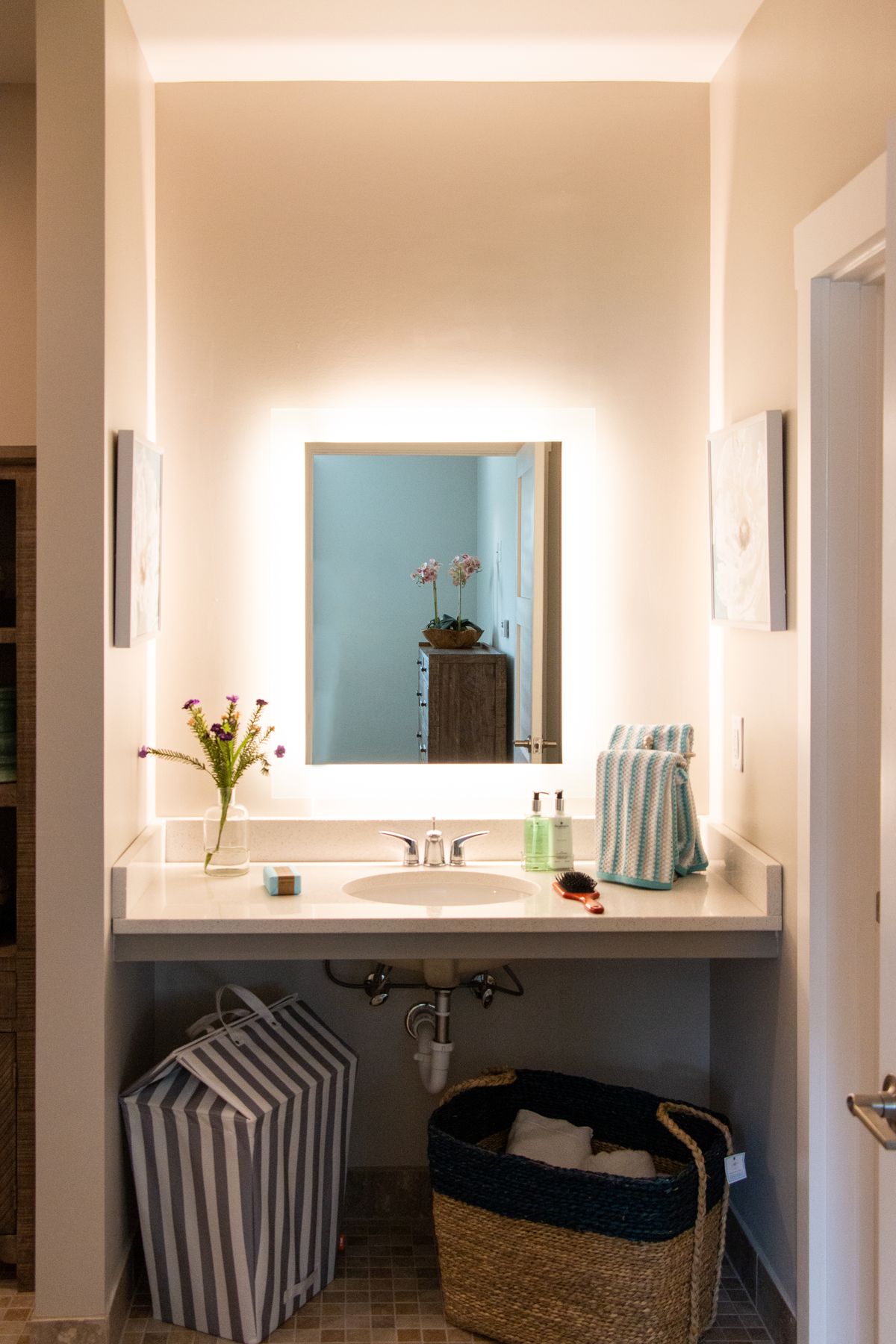 A well-lit bathroom vanity with a mirror, fresh flowers, and neatly arranged towels.