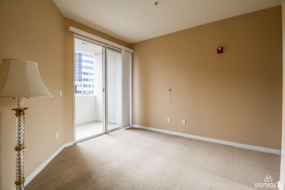 An empty room featuring beige walls and a carpeted floor, with a sliding glass door allowing natural light to enter.