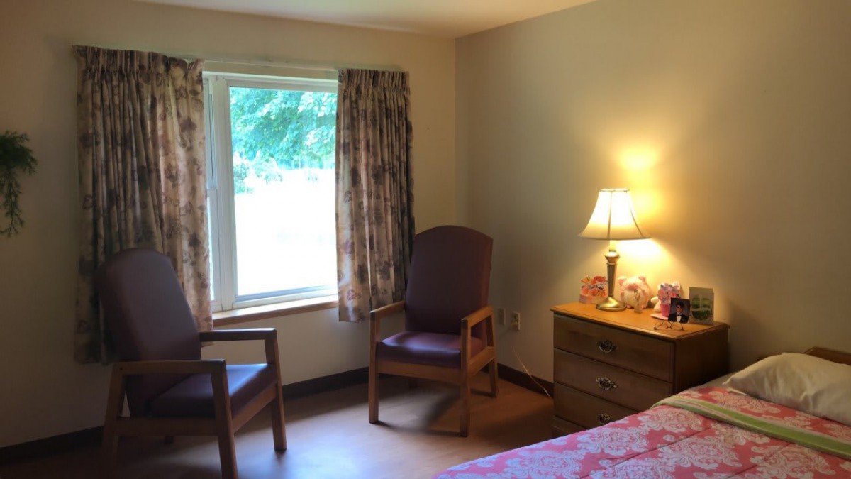 A cozy room with a window, two chairs, and a lamp on a dresser.