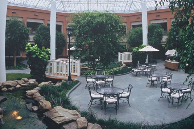 A serene indoor atrium featuring tables and chairs surrounded by lush greenery under a glass ceiling.