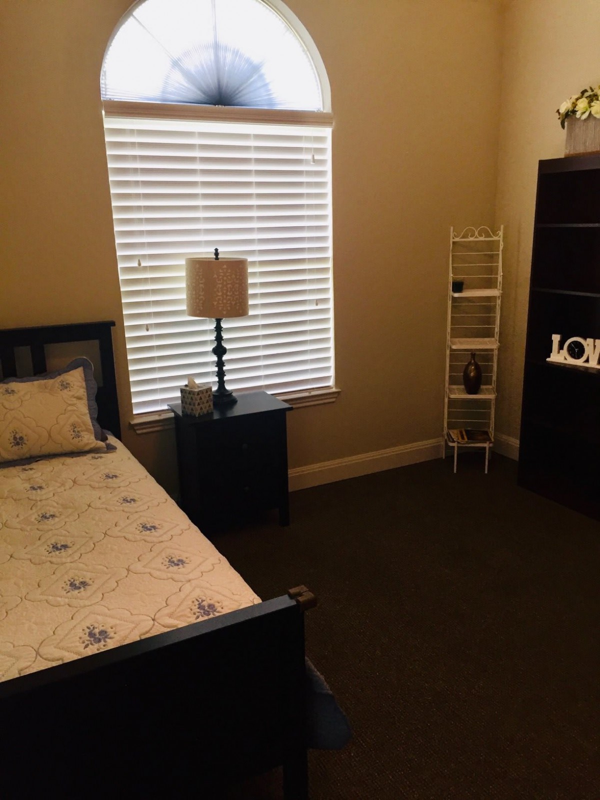 A cozy bedroom with a single bed, lamp, and shelving unit.