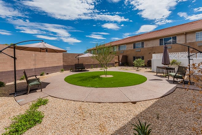A well-maintained backyard with artificial grass, patio seating, and desert landscaping on a sunny day.